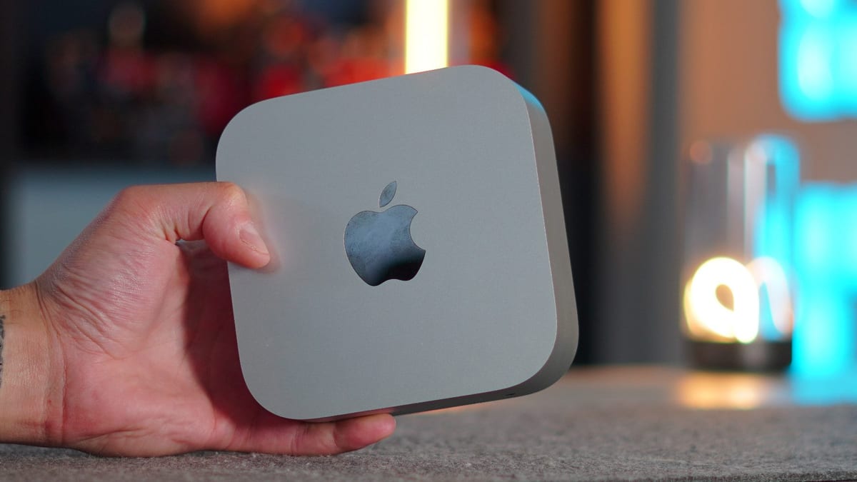 Fotografía de una Mac mini de Apple, computadora compacta en forma de caja plateada, colocada sobre una superficie clara, mostrando su carcasa de aluminio y puertos frontales.